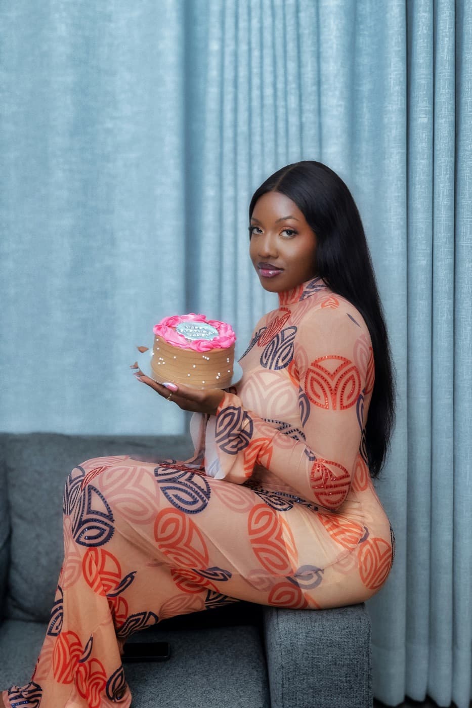 A smiling young woman holding a decorated cake she made, in Accra